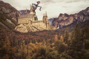 #pracegover audiodescrição resumida: paisagem de dia. Ao fundo, monte com castelo de hogwarts. Em uma das torres do castelo há um dragão. À frente, floresta.